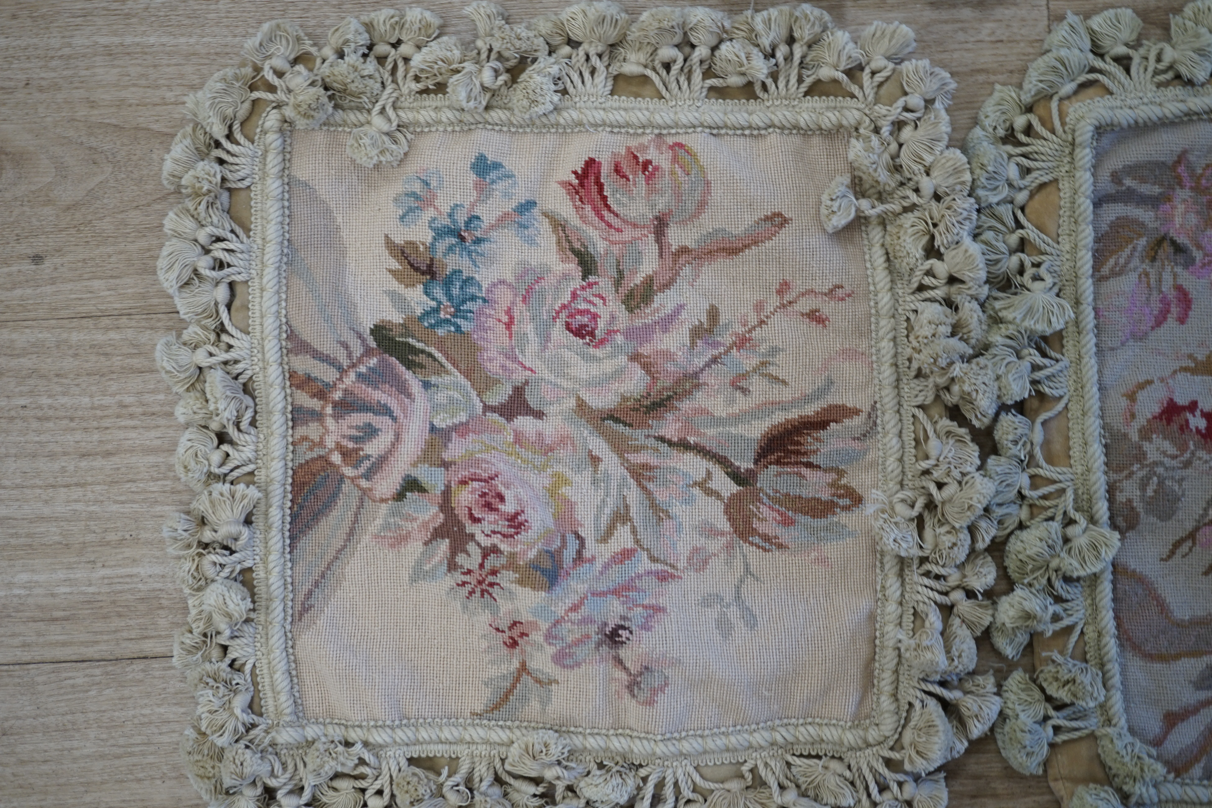 Three small square rose designed wool worked cushion covers and one similar larger cushion cover all with cotton tasselled edging, smaller covers 38cm square, larger cover 38cm x 48cm. Condition - good